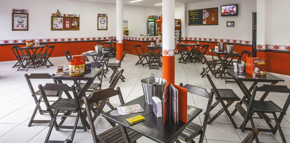 Salão de um bar parceiro com mesas, cardápios e materiais das marcas
